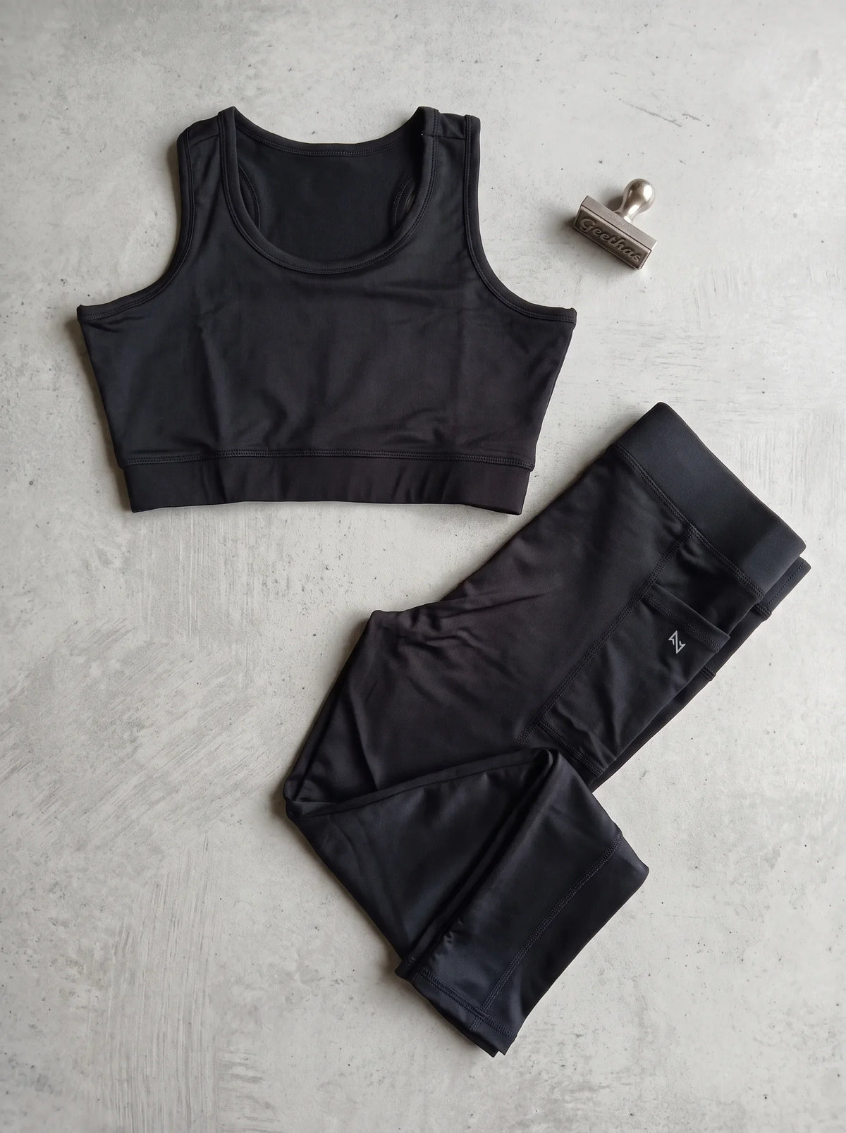 Black sleeveless gym crop top and matching pocket-detail leggings displayed flat