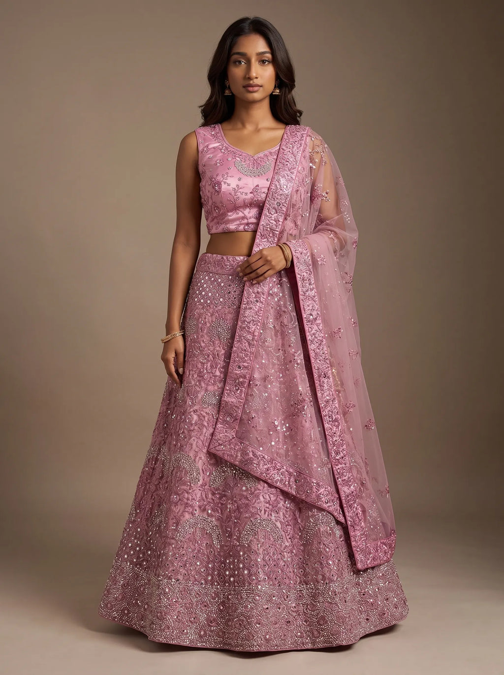 Model wearing dusty pink floral embroidered net lehenga set with matching bordered dupatta