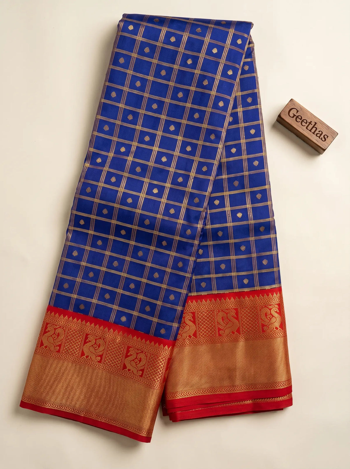 Royal blue soft silk saree displayed flat with gold-toned grid motifs and a red woven border
