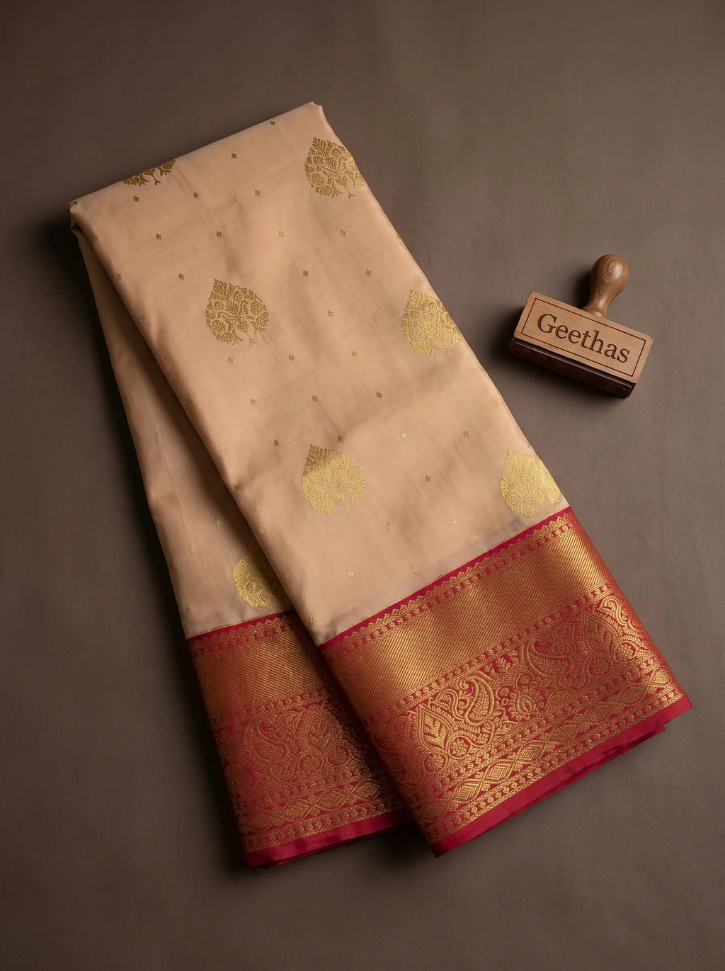 Folded light peach soft silk saree showing gold-toned woven leaf motifs and ornate magenta zari border