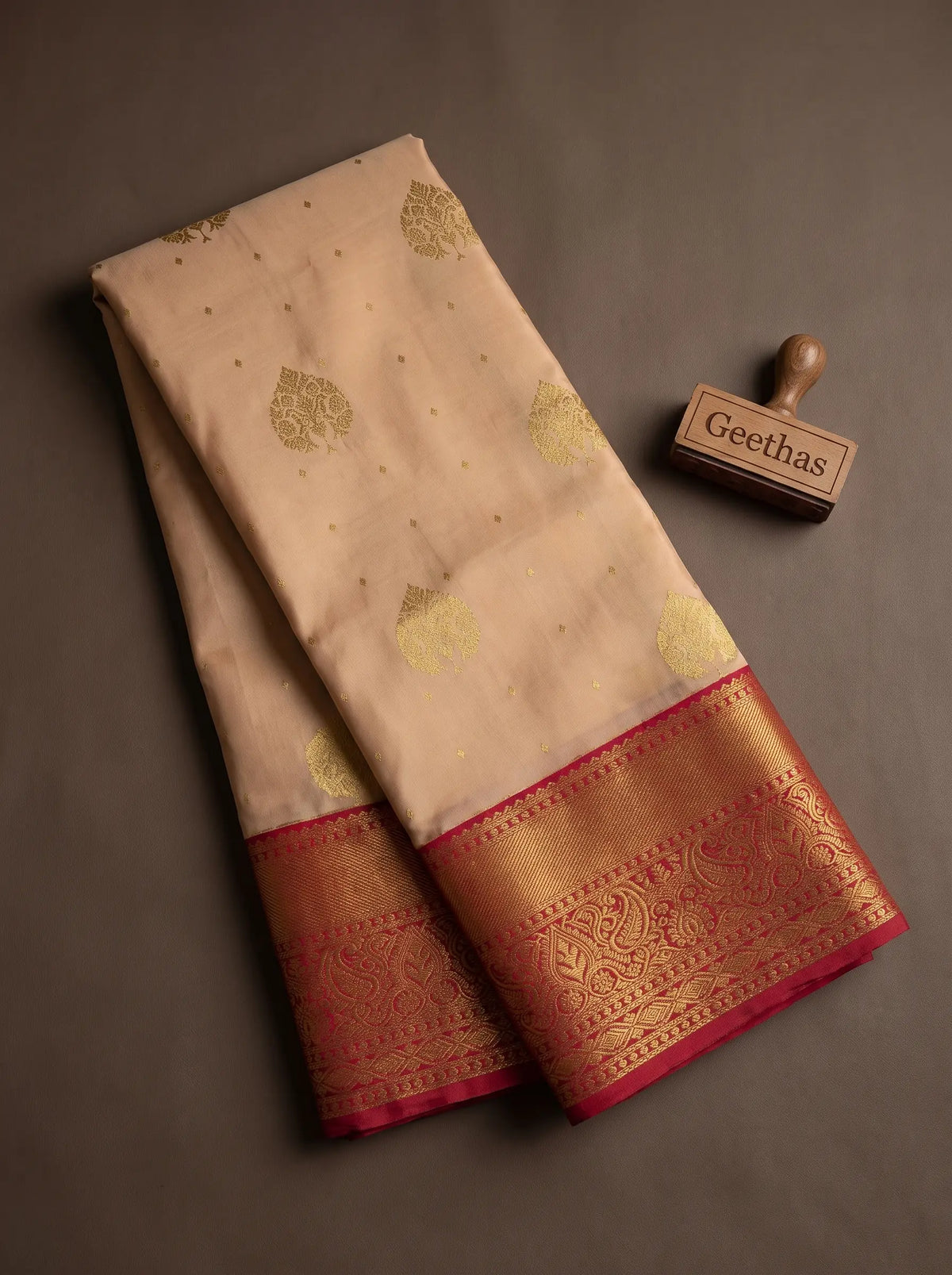 Folded light peach soft silk saree showing gold-toned woven leaf motifs and ornate magenta zari border
