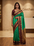 Model wearing bottle green soft silk saree with a deep maroon patterned border and pallu