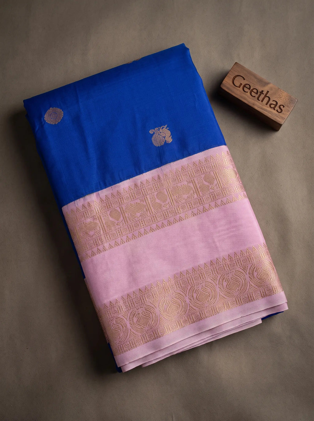 Folded royal blue soft silk saree with lilac woven zari border and gold-toned motifs