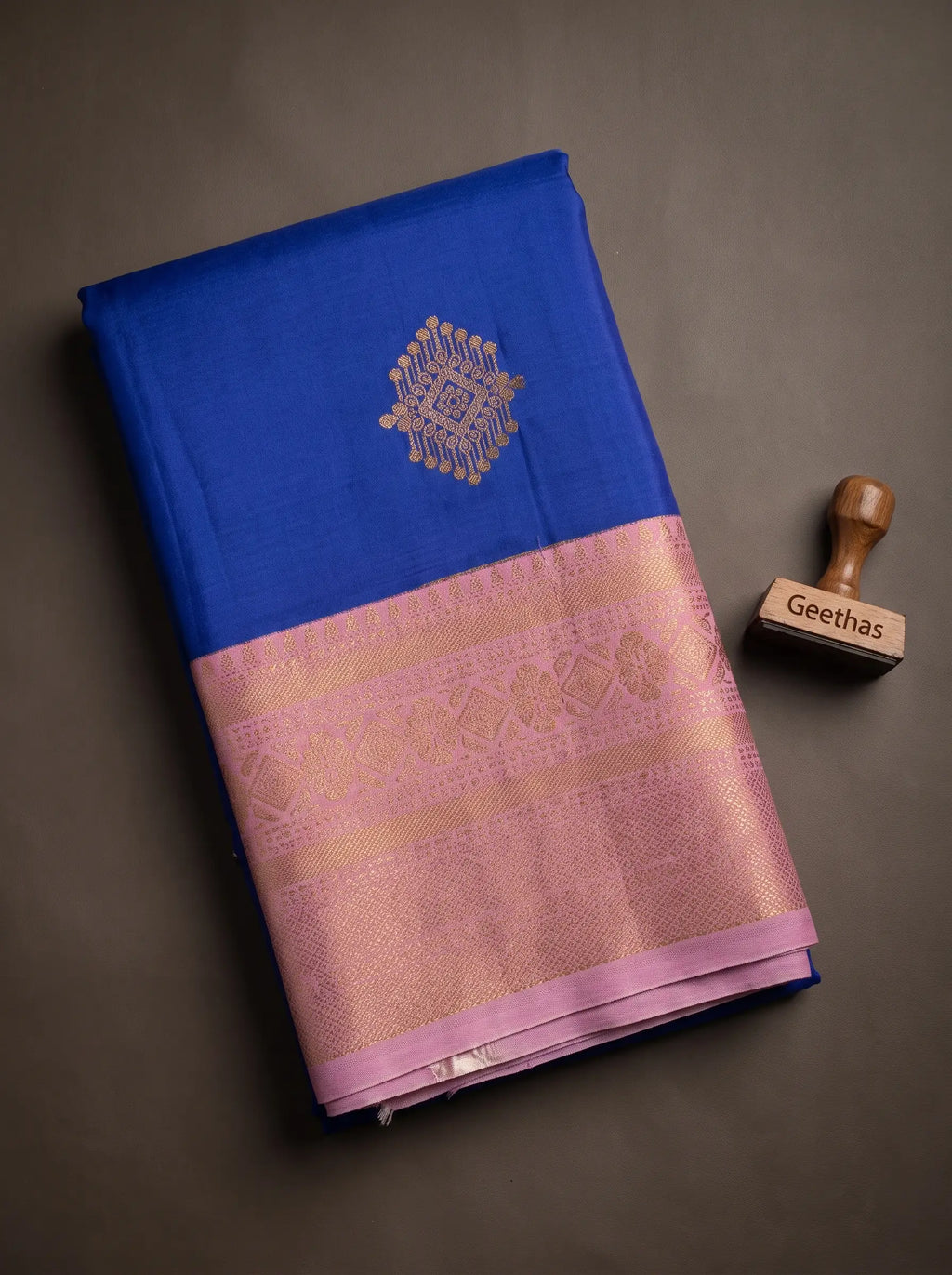 Folded royal blue soft silk saree showing gold-toned woven motif and pink patterned border