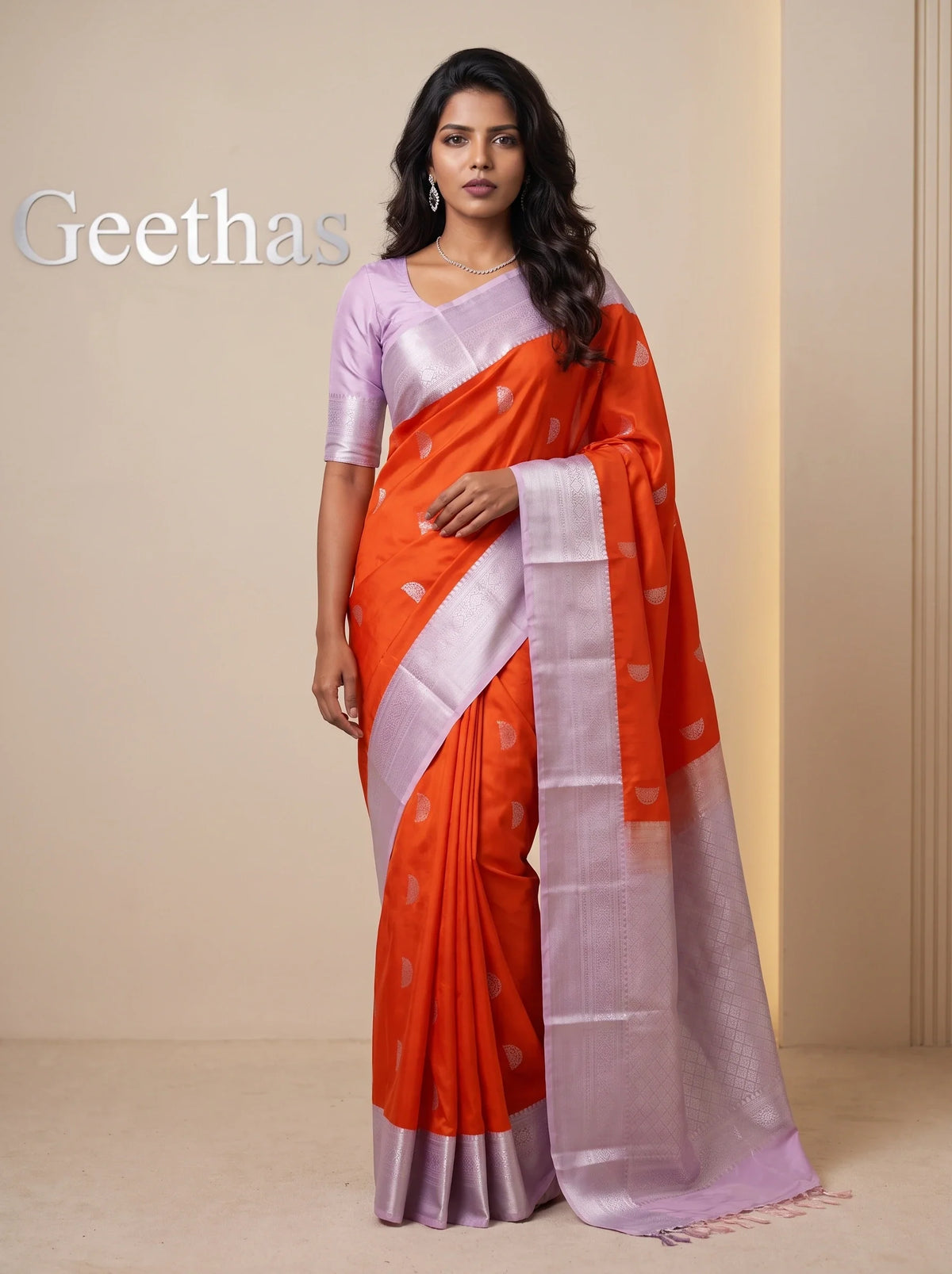 Model wearing a vermilion orange soft silk saree with woven motifs and a contrasting lavender-toned border and pallu.