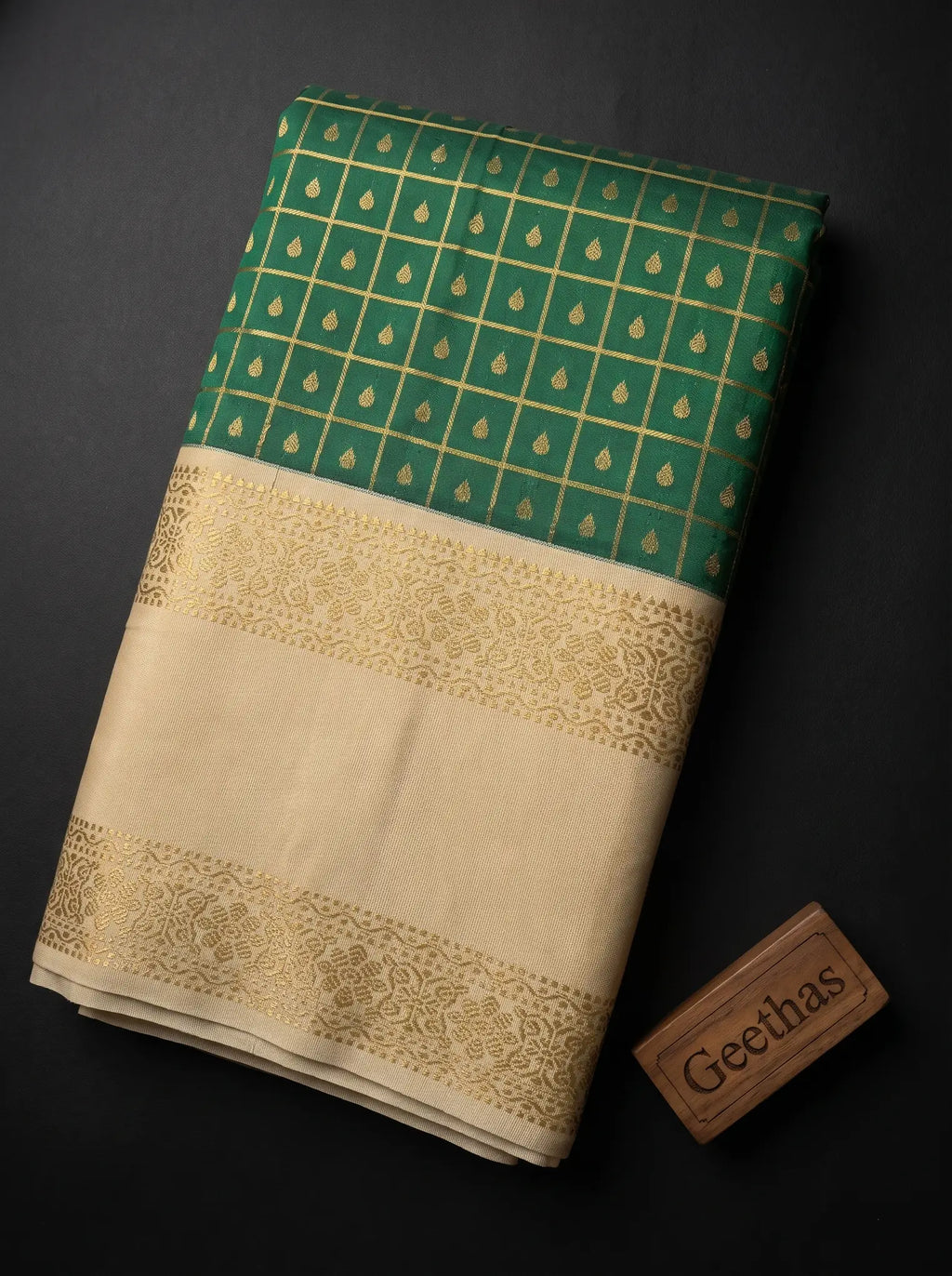 Folded deep green soft silk saree showing gold-toned grid motifs and an ivory-beige decorative woven border